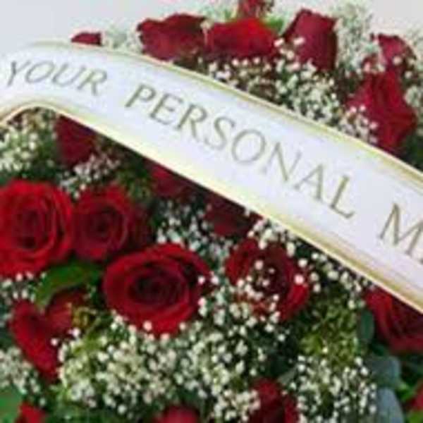 Red rose funeral spray with a white ribbon reading personal message
