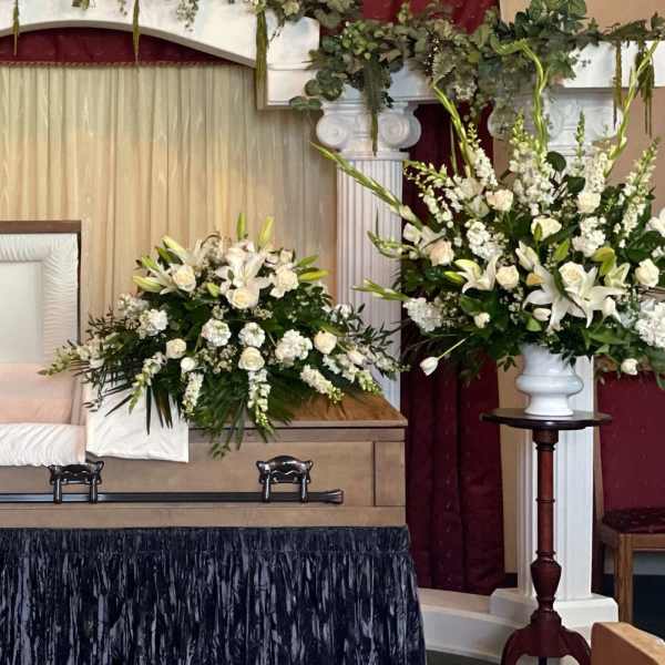 Sympathy casket spray with white lilies and roses beside an open casket
