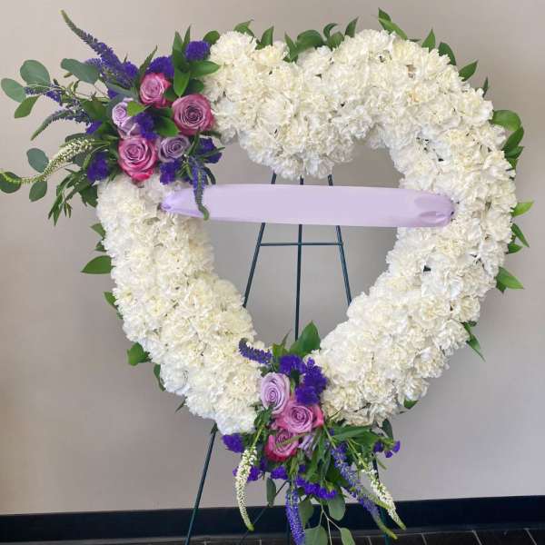 Heart-shaped white floral wreath with pink and purple roses on an easel