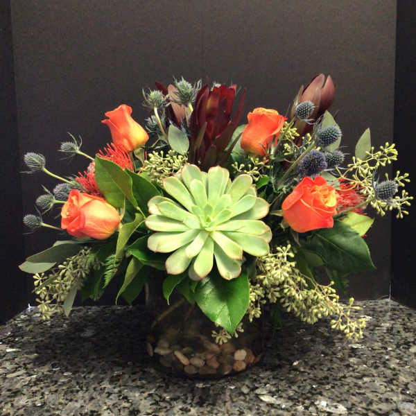 Orange roses and succulents arranged in a dark glass vase