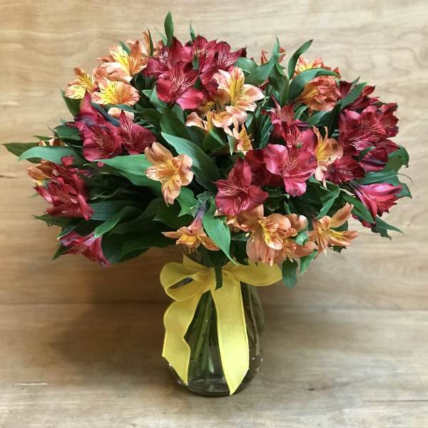 Bouquet of red and peach flowers in a glass vase with a yellow ribbon