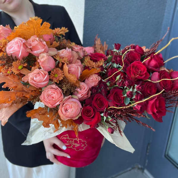 Large bouquet of pink and red roses with autumn leaves in a red box