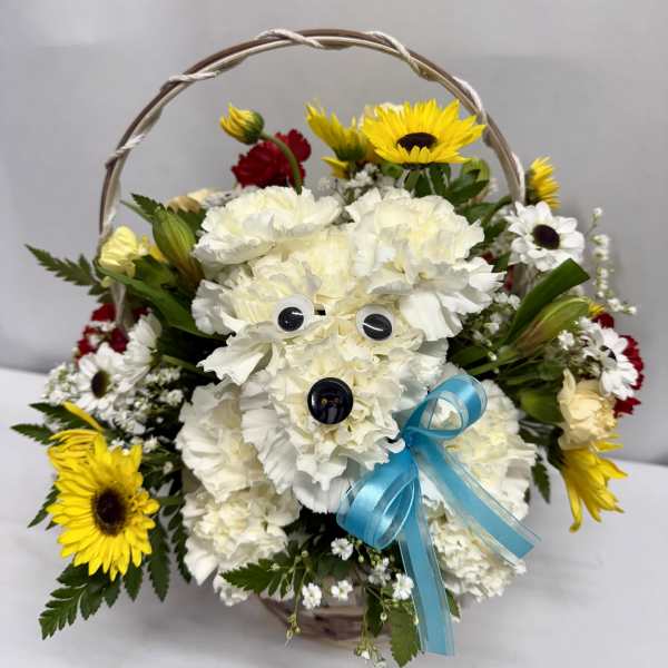 Basket arrangement with white carnation dog, yellow sunflowers, red and white daisies and a blue bow