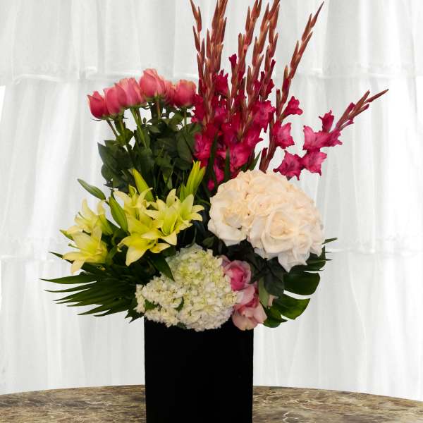 Tall floral arrangement with pink, yellow, white, and red blooms in a black vase