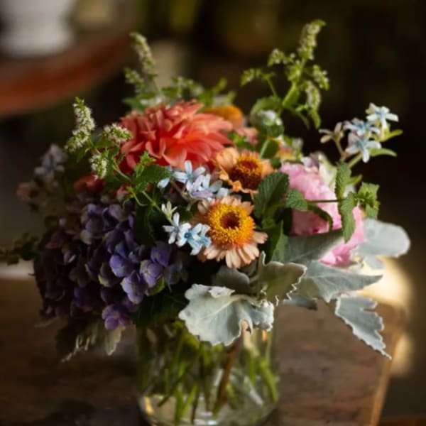 Mixed bouquet in a clear glass vase with pink, orange, purple, and blue flowers