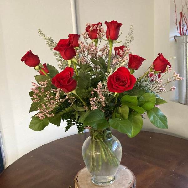 Red roses arranged in a clear glass vase on a wood slice base