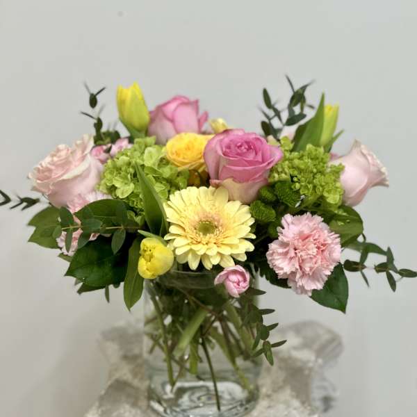 Mixed pink and yellow flowers arranged in a glass vase