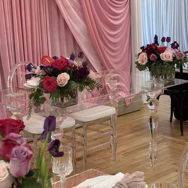 Pink and purple floral centerpieces on clear acrylic tables with draped pink fabric backdrop