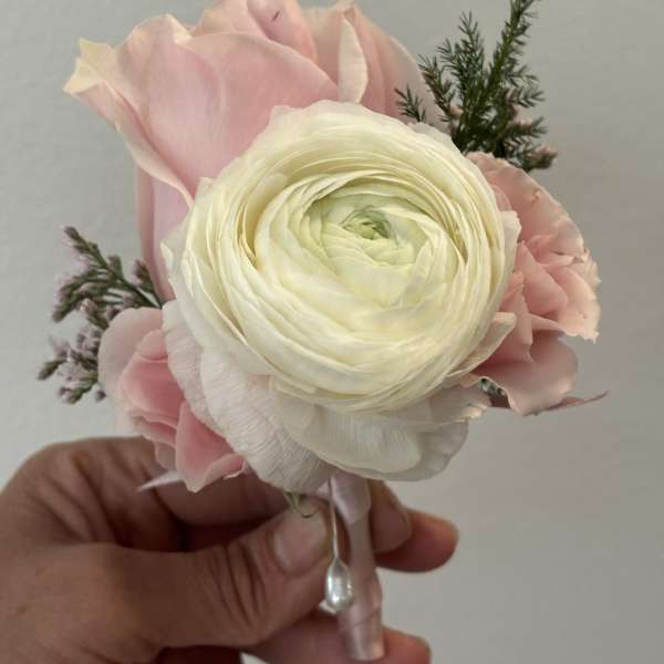 Small pink and white floral boutonniere held in a hand