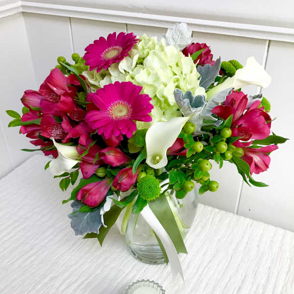 Mixed bouquet of hot pink gerbera daisies, white hydrangea, and mini calla lilies in a clear glass vase.