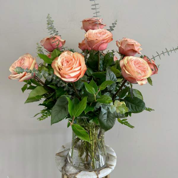 Peach roses arranged in a clear glass vase with greenery.