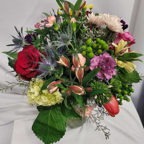 Mixed bouquet of roses, carnations, and lilies in a glass vase