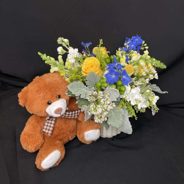 Bouquet of yellow, blue, and white flowers beside a teddy bear