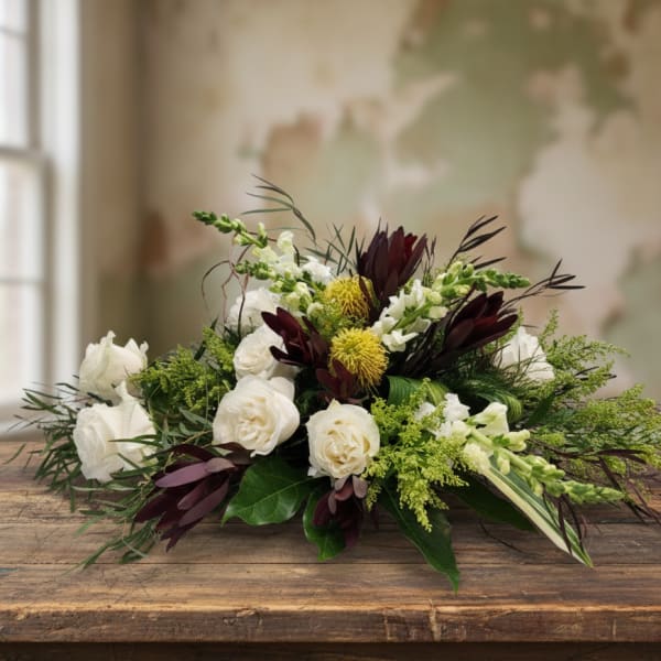 Low centerpiece of white roses, green accents, and dark burgundy blooms in an elongated design