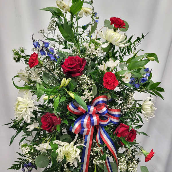 Standing floral spray with red roses, white lilies, and a red-white-blue ribbon