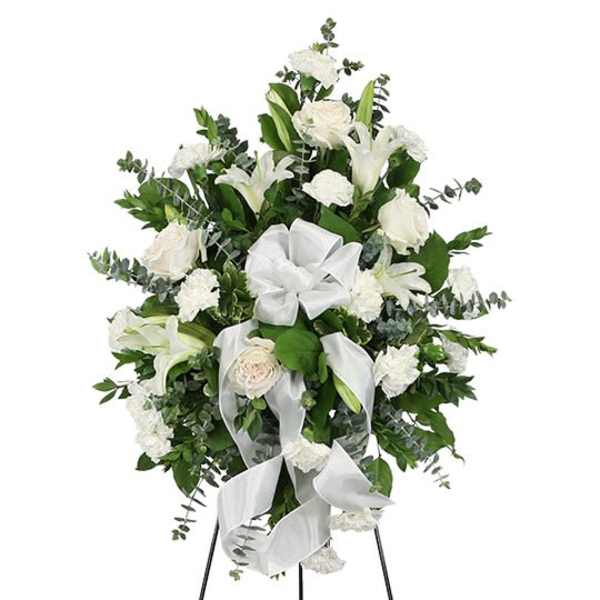 White floral standing spray with lilies, roses, and ribbon on an easel