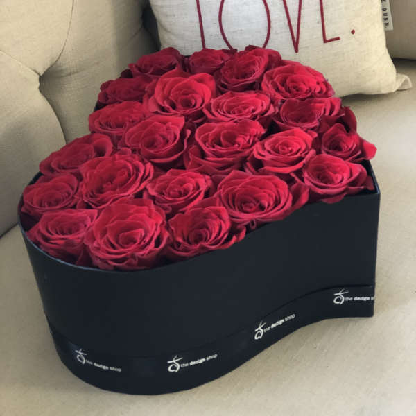 Heart-shaped box of red roses beside a pillow with the word LOVE