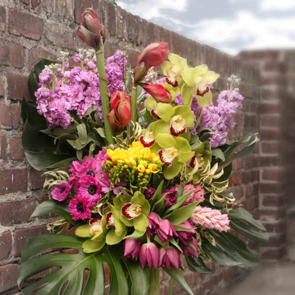 Tall tropical bouquet in a clear vase with orchids, lilies, and pink blooms