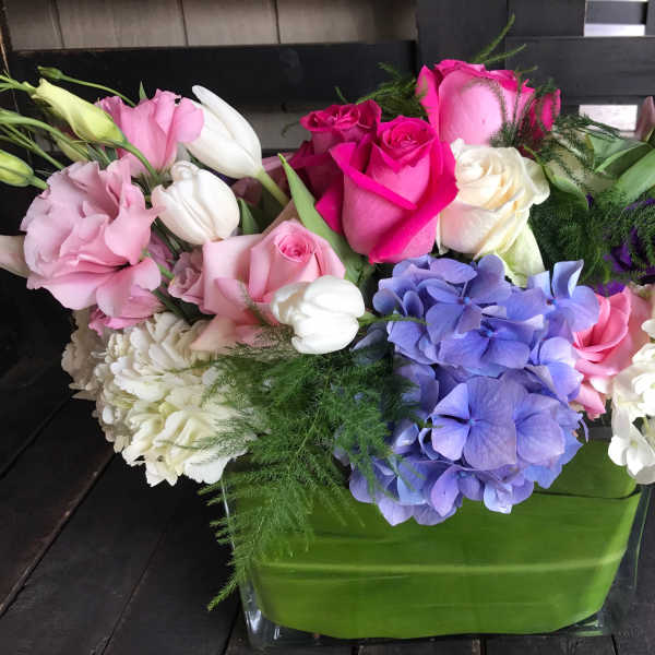 Mixed bouquet of roses, hydrangeas, tulips, and lilies in a green vase