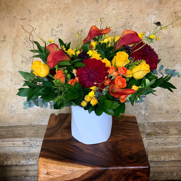Colorful floral arrangement in a white vase with yellow, orange, and burgundy blooms