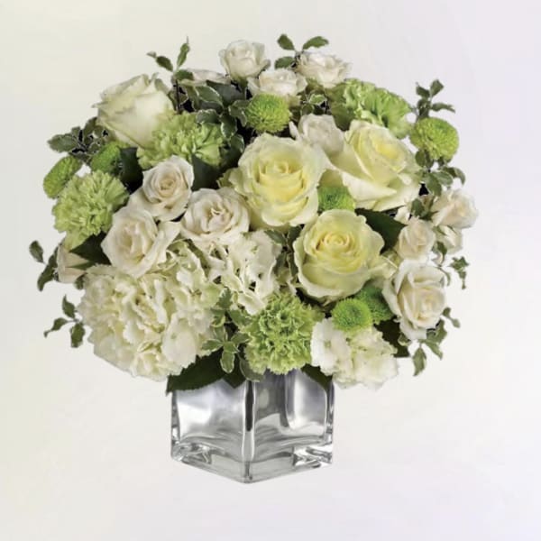 White and pale green floral arrangement in a clear square vase
