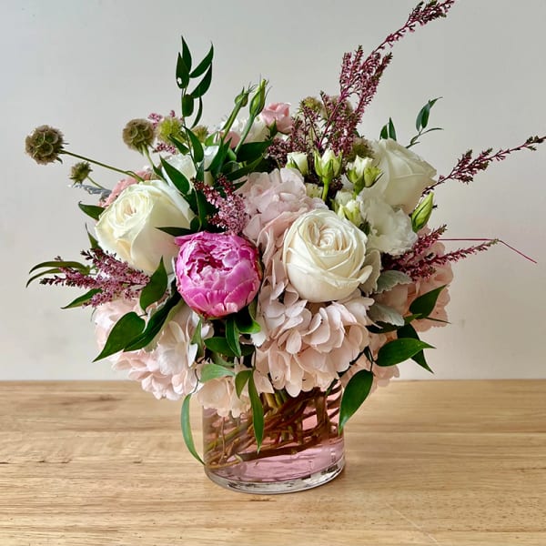 Round arrangement of pink hydrangeas, white roses, and a pink peony in a clear glass vase