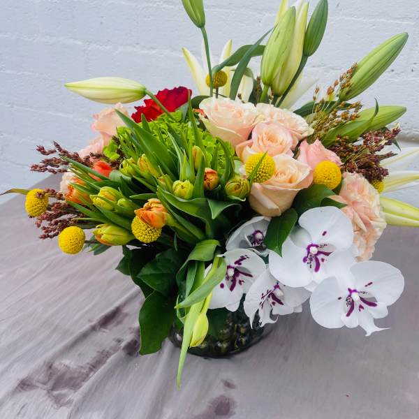 Mixed bouquet with lilies, roses, and white orchids in a glass vase