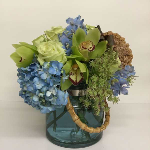 Blue hydrangeas and green orchids arranged in a glass vase