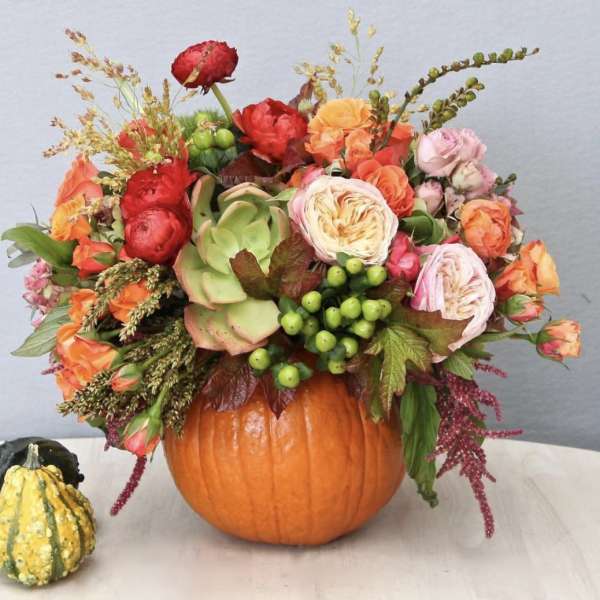 Floral arrangement in a pumpkin vase with orange, pink, and red blooms