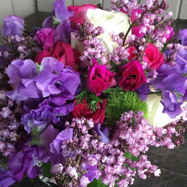 Bouquet of pink, purple, and white roses with lilac blossoms in a green vase