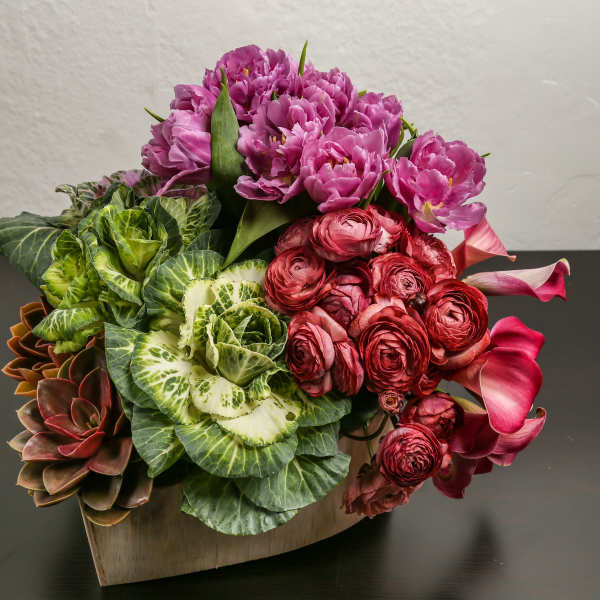 Pink flowers arranged with green ornamental cabbage in a wooden container