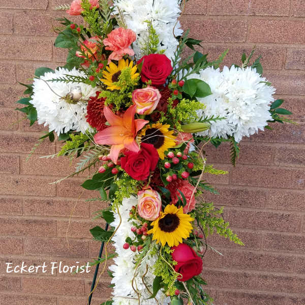 Standing floral cross with white chrysanthemums, red roses, and sunflowers