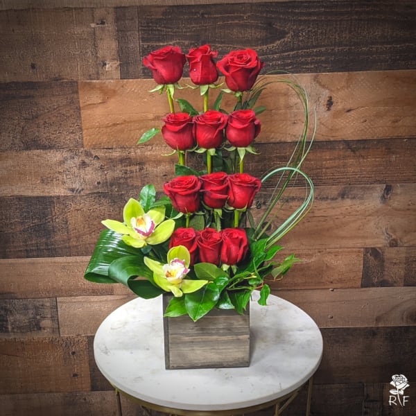 Tall arrangement of red roses with yellow orchids in a square wooden vase