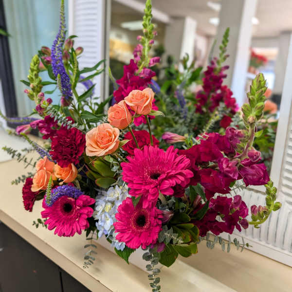 Bright arrangement of hot pink gerbera daisies, peach roses, and burgundy snapdragons with blue hydrangea accents