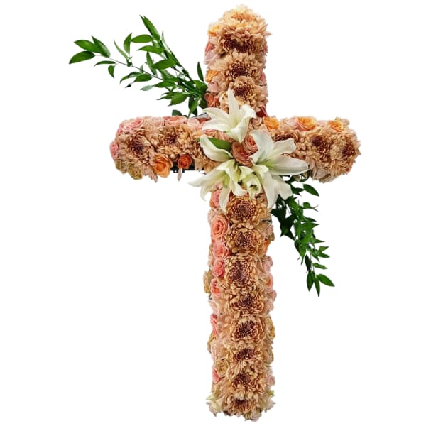 Floral cross covered in peach and cream flowers with white lilies and greenery
