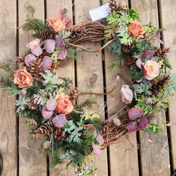 Floral wreath with peach roses, pinecones, and mixed greenery on a wooden surface