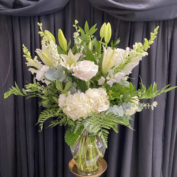 White floral arrangement in a glass vase on a gold pedestal stand
