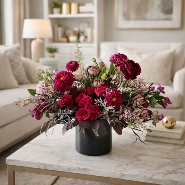 Pink and burgundy flower arrangement in a black vase on a coffee table