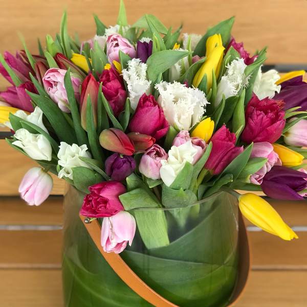 Mixed tulip bouquet in a green glass vase with a tan handle