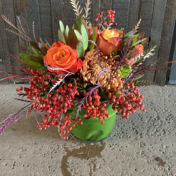 Orange roses and mums in a green vase with red berries