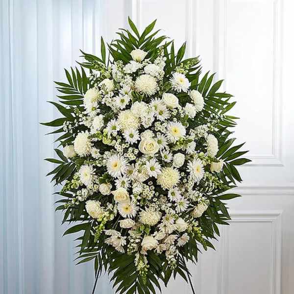 Large white funeral spray with mixed blooms and palm leaves on an easel