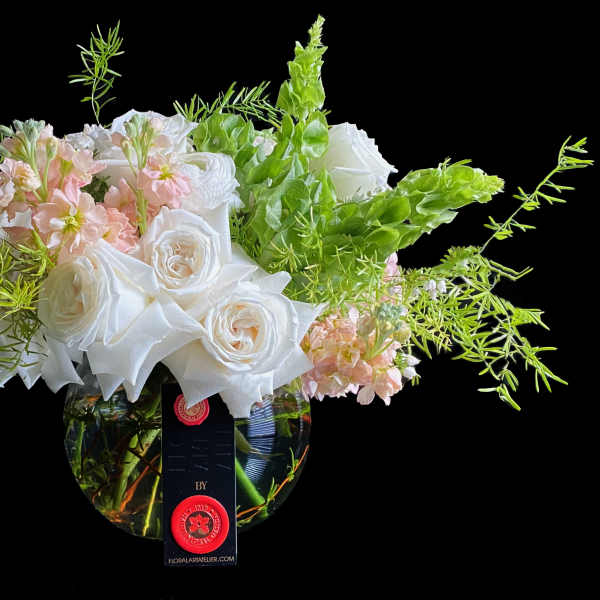 Low round arrangement of white roses and soft pink flowers in a clear bowl vase with airy greenery.
