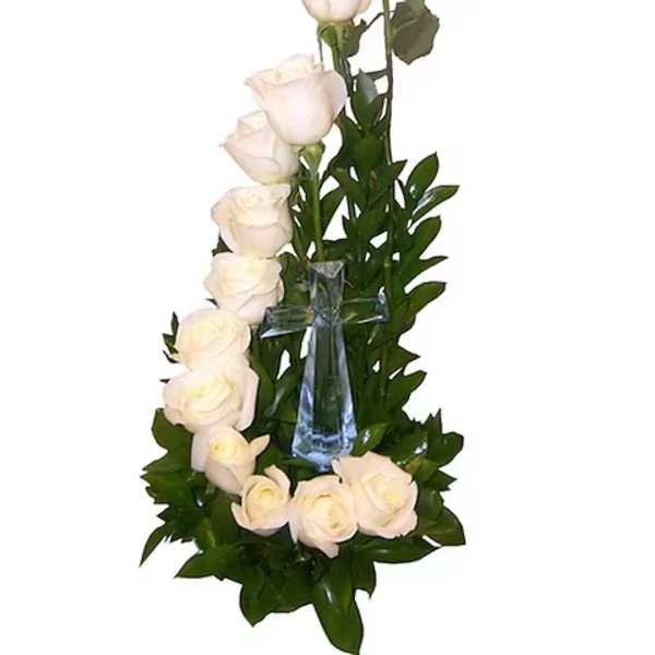 White roses arranged around a clear glass cross with greenery