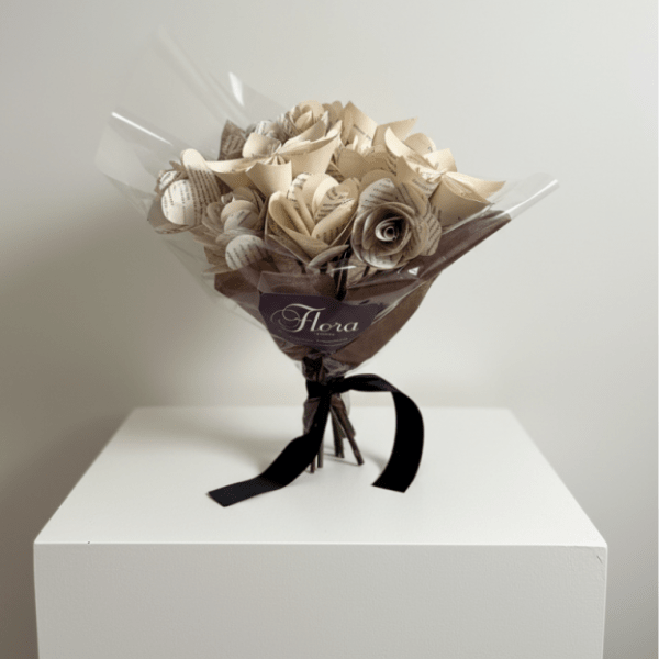 Bouquet of cream paper roses made from printed pages, wrapped in cellophane with brown paper and a black ribbon.