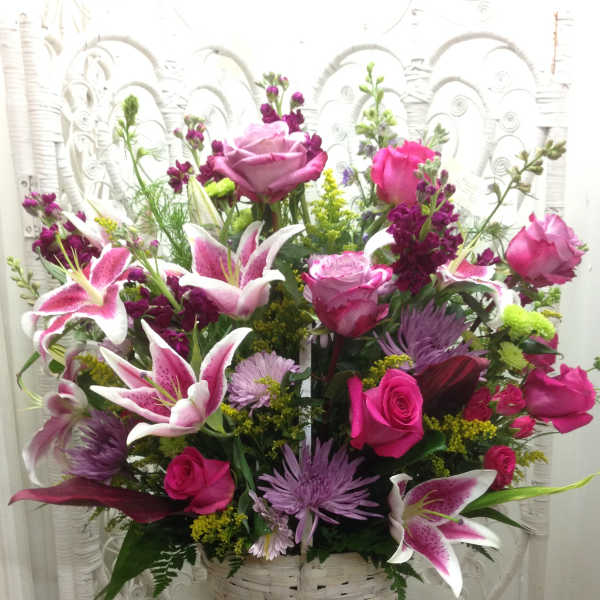 Basket arrangement of pink roses, lilies, and purple flowers