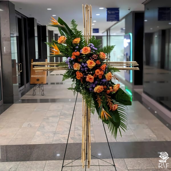 Tall floral standing cross with orange roses and tropical blooms