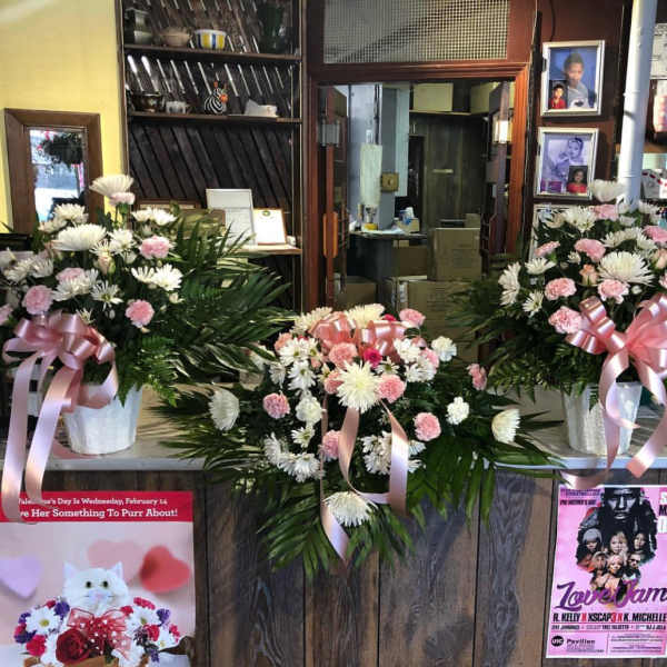 Three pink and white floral arrangements with ribbons in white containers