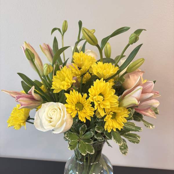 Bouquet of yellow chrysanthemums, pink lilies, and a white rose in a glass vase