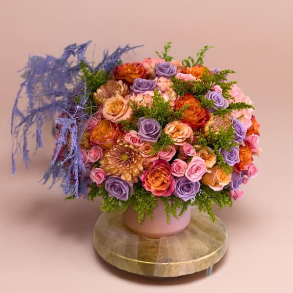 Round bouquet of pink, lavender, and orange roses in a pink vase