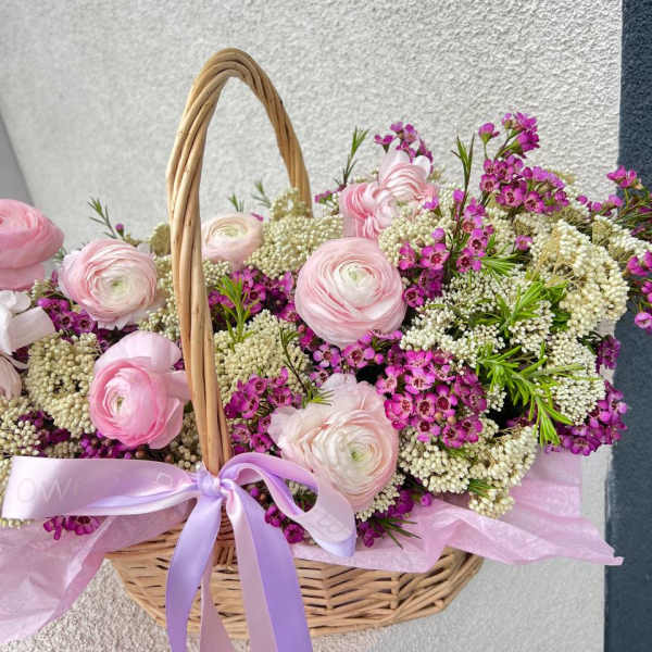 Pink and white flowers arranged in a wicker basket with a lavender ribbon